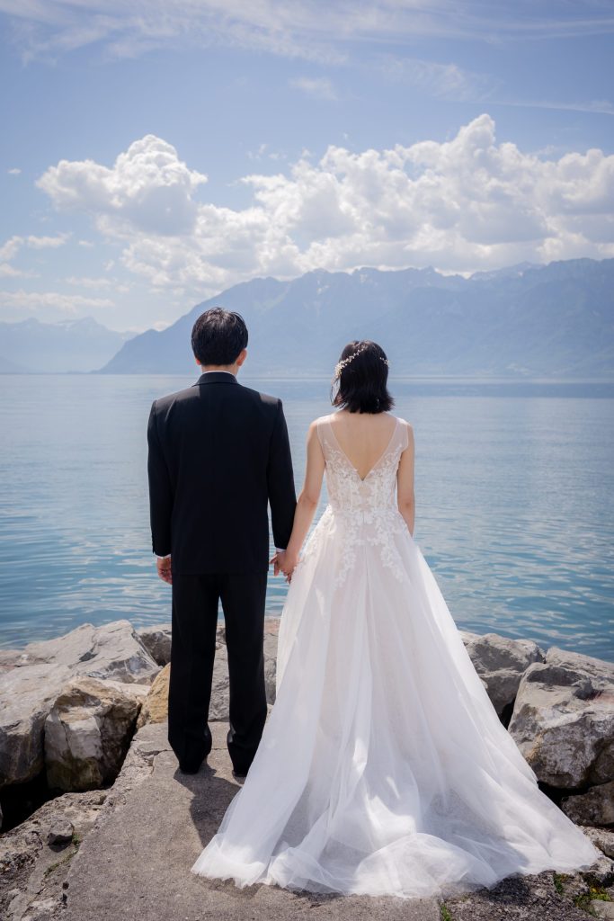 Bride and groom on the rocks at the lake edge, the Alps across the water