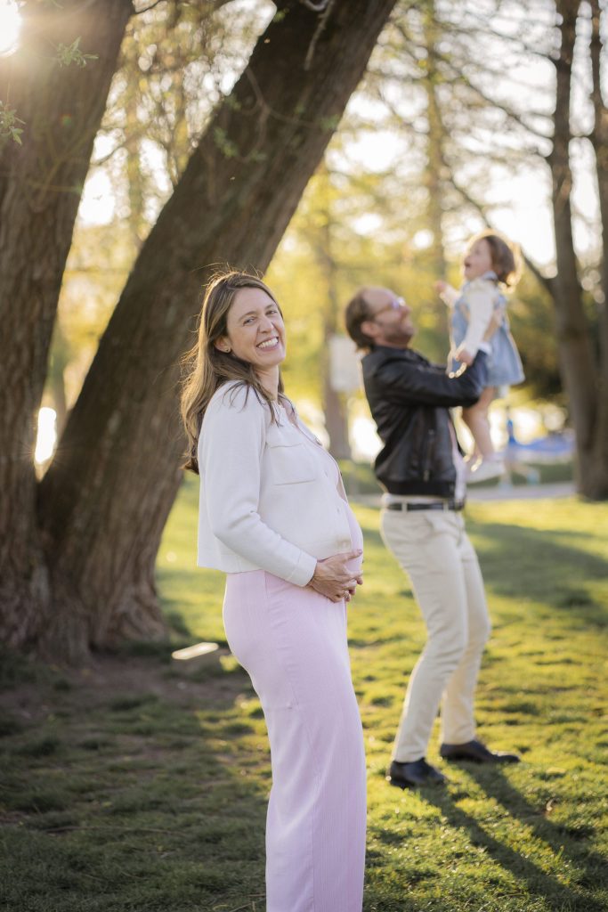 Expecting mother in a park, her partner lifting their child behind her